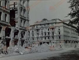 V a/10. 20 años después: La imagen enseña los destrozos del centro de Viena. En primer plano, el edificio (con reloj) que fue cuartel general de la Gestapo, en Morzinplatz.